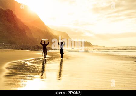 Surfer Silhouettes sulla spiaggia all'ora del tramonto. Amici surfisti che portano le loro tavole da surf all'ora del tramonto. Foto Stock