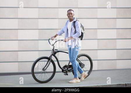 Bel ragazzo nero con zaino e moto moderna vicino mattone muro sulla strada della città Foto Stock