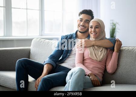 Coppia araba positiva seduta sul divano a casa Foto Stock