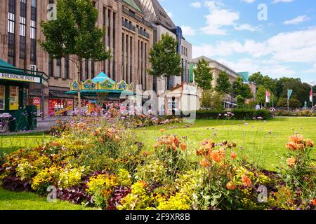 Vista panoramica di Corneliusplatz nel centro di Düsseldorf con giostra nostalgica di fronte all'edificio del grande magazzino 'Kaufhof', costruito nel 1909. Foto Stock