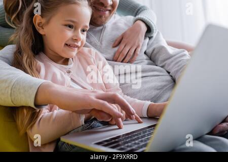 Sorridente bambino che usa un computer portatile vicino ai genitori su sfondo sfocato Foto Stock