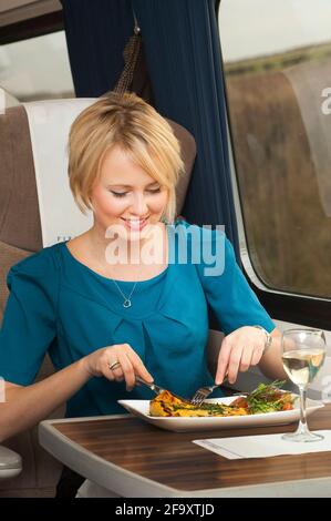 Giovane donna che ama il pranzo mentre viaggia in una carrozza di prima classe su un treno nel Regno Unito. Foto Stock