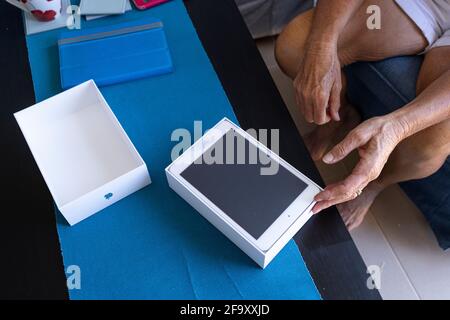 Donna anziana che sboxe un nuovo mini tablet Apple ipad nel suo soggiorno. Foto Stock