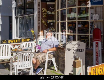 Idea di staycation. Uomo che fuma pipa seduto ad un tavolo fuori dal tabacchista & Cigar Merchant, George Street, Old Town Hastings UK, in una giornata estiva. Foto Stock