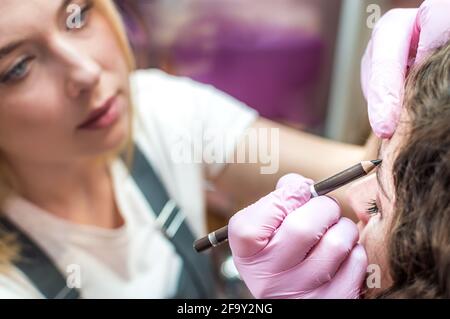 Ritratto di giovane bella ragazza le cui sopracciglia sono strappate. Sopracciglia che si forma in un salone di bellezza. Primo piano di sopracciglia e mano di artista sopracciglia Foto Stock