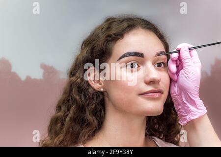 Ritratto di giovane bella ragazza le cui sopracciglia sono strappate. Sopracciglia che si forma in un salone di bellezza. Primo piano di sopracciglia e mano di artista sopracciglia Foto Stock