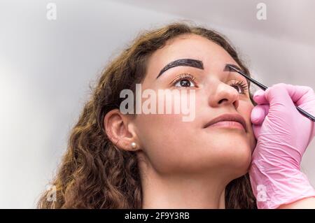 Ritratto di giovane bella ragazza le cui sopracciglia sono strappate. Sopracciglia che si forma in un salone di bellezza. Primo piano di sopracciglia e mano di artista sopracciglia Foto Stock