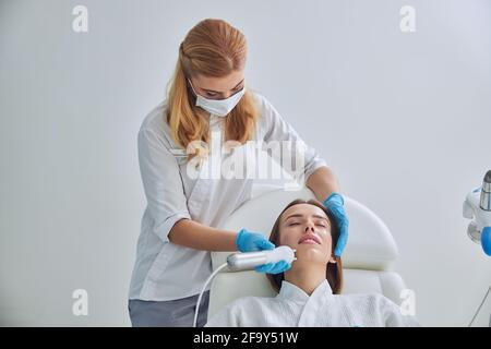 Giovane adorabile donna decapitata in accappatoio bianco ricevendo professionale anti procedura di invecchiamento della pelle in clinica di bellezza Foto Stock