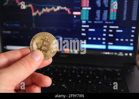 Uomo in possesso di una versione fisica di Bitcoin BTC. In background sono i dati che analizzano in borsa. Foto Stock