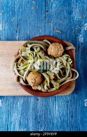vista ad alto angolo di un piatto di terracotta con alcune tagliatelle di farro con polpette di kale e vegan, su un rustico tavolo di legno blu Foto Stock