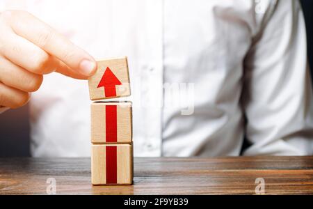 L'uomo raccoglie una torre di blocchi con una freccia. Crescita graduale della carriera. Concetto di sviluppo a nuovi livelli. Espansione aziendale. Miglioramento delle qualifiche Foto Stock