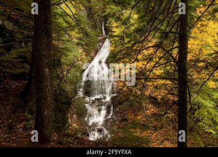 Una vista di Moss Glen Falls, una cascata in Vermont, Stati Uniti, preso da una distanza attraverso gli alberi in autunno / caduta Foto Stock