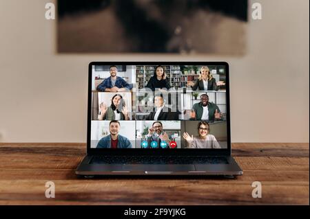 Vista frontale sullo schermo del computer portatile su una scrivania in legno, con un gruppo di persone diverse multirazziali che comunicano tramite videoconferenza, riunione aziendale online virtuale di partner di successo, videochiamata Foto Stock