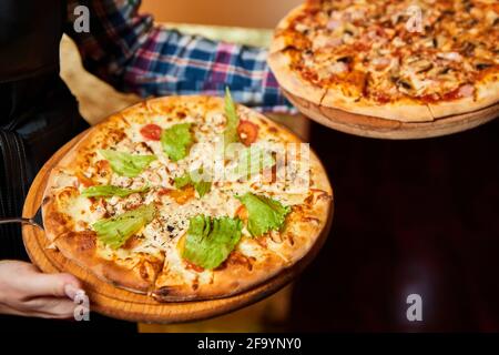 Il cameriere tiene in mano due pizze su tavole di legno. Primo piano, messa a fuoco selettiva Foto Stock