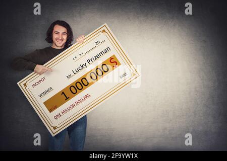 Uomo eccitato che tiene un assegno bancario vincitore della lotteria. Jackpot felice ragazzo vincendo un milione di dollari premio. Grande banner che annuncia il premio principale. Ricchezza, lu Foto Stock