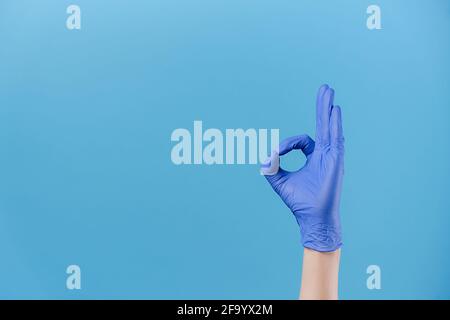 Primo piano della mano maschile in guanti di protezione medica dimostra ok segno, isolato in sfondo blu studio con spazio di copia, esprime la celebrazione Foto Stock