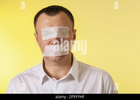 Un uomo con gli occhi e la bocca sigillati con un nastro di pittura su uno sfondo giallo, il concetto non ha paura di dire la verità. Foto Stock
