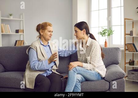 Madre anziana che parla con la sua giovane figlia cresciuta mentre si siede sul divano a casa Foto Stock