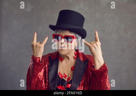 Simpatica signora anziana con capelli grigi in top Hat che mostra rock-n-roll segnale a mano Foto Stock