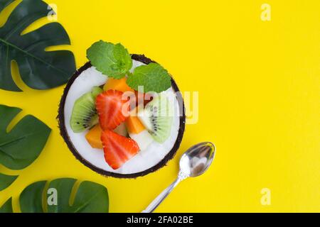 Insalata di frutta nella metà di cocco su sfondo tropicale. Vista dall'alto.Copia spazio. Foto Stock