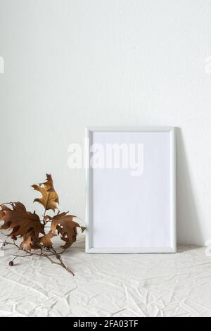 Casa decoratore moccap, quadro vuoto cornice vicino bianco dipinto muro di cemento, rami con foglie asciutte Foto Stock