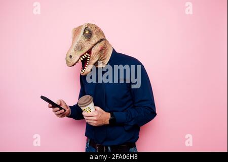 Uomo a testa di dinosauro con una tazza di caffè e uno smartphone. Foto Stock