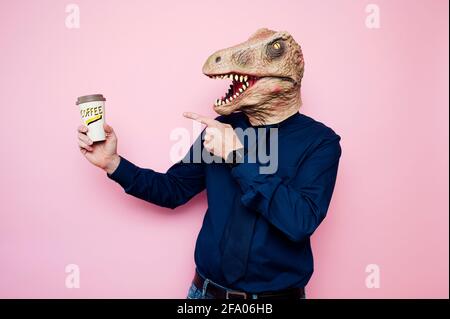 Uomo a testa di dinosauro che indica una tazza di caffè in cartone riciclabile. Foto Stock