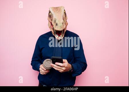 Uomo a testa di dinosauro con una tazza di caffè e uno smartphone. Foto Stock