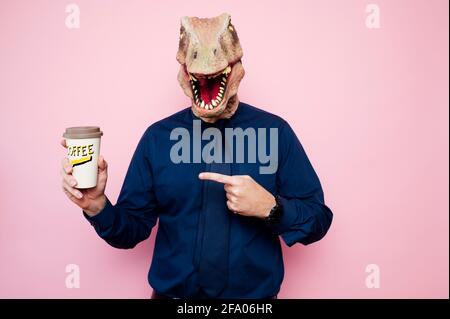 Uomo a testa di dinosauro che indica una tazza di caffè in cartone riciclabile. Foto Stock