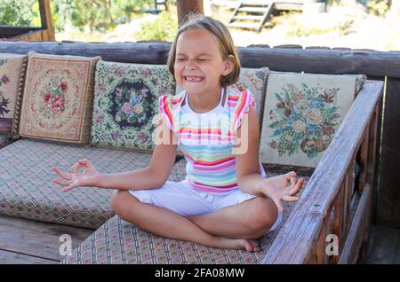 Ragazza divertente senza un dente anteriore nella posizione del loto cerca il suo meglio per meditare. Foto Stock