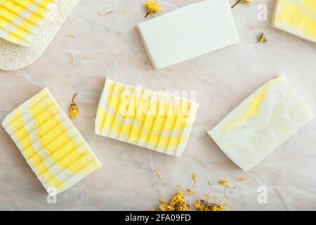 Saponette di oliva naturale modello con erbe fiori di marigold secco. Molti saponi da bar fatti in casa bianchi, prodotti da bagno spa per la cura della pelle del corpo. Piatto posare Foto Stock