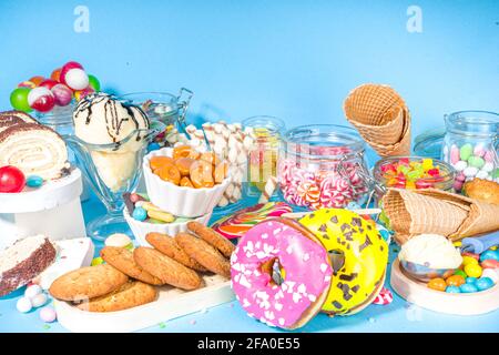 Selezione di dolci colorati. Set di caramelle, cioccolatini, ciambelle, biscotti, lecca, gelateria vista dall'alto su uno sfondo trendy e soleggiato di colore blu brillante Foto Stock