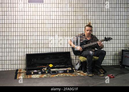 Brisbane Australia 8 5 2015 giovane uomo con un uomo e jeans strappati suona la chitarra elettrica per suggerimenti in metropolitana allestita da parete di piastrelle sporche. Foto Stock