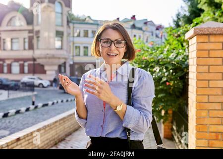 Positivo sorridente donna di affari matura che indossa occhiali blu camicia cercando alla telecamera Foto Stock