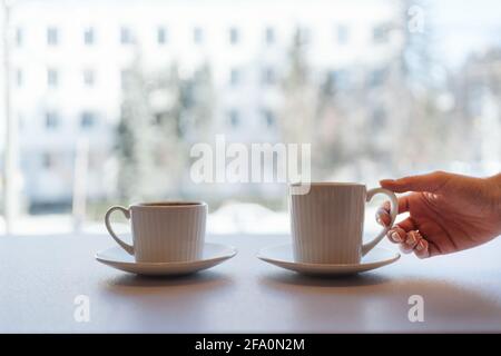 Soglia della finestra dell'ufficio, caffè con vista sulla città e due tazze con tè o caffè tazze nella prima colazione del mattino. Mano della donna che prende una tazza Foto Stock