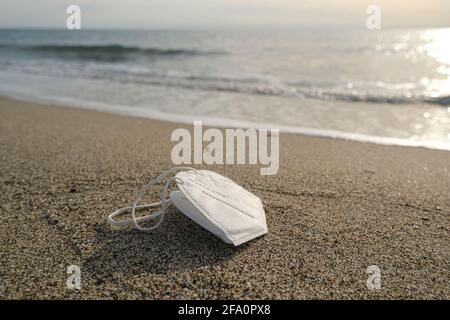 Gettato maschera monouso galleggiando sulla riva del mare sporco, covid19 pandemia inquinamento Foto Stock