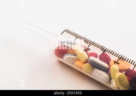Siringa riempita con pillole di medicina assortite su sfondo bianco Foto Stock