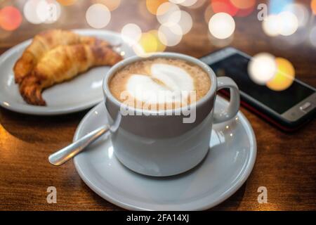 Caffè latte con croissant grassi e cellulare. Foto Stock