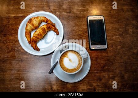 Caffè latte con croissant grassi e cellulare. Foto Stock