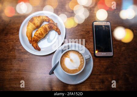 Caffè latte con croissant grassi e cellulare. Foto Stock