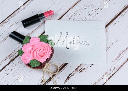 Cupcake di velluto rosso con glassa di crema al burro, accanto a un rossetto. In background nota scritta madre. Foto Stock