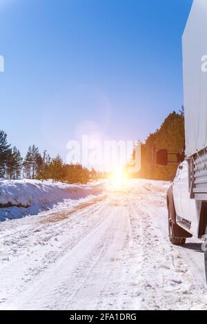 Auto bianca su una strada invernale attraverso una foresta innevata. Vista dal basso. Auto su strada innevata invernale in montagna in giornata di sole. Foto Stock