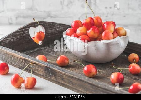 Ciotola bianca con ciliegie dolci arancioni mature di tipo "anna reale" su un vassoio di legno, sfondo bianco Foto Stock