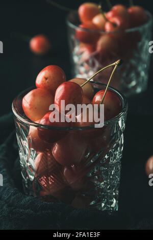 Ciliegie dolci d'arancio mature della specie 'anna reale' in un bicchiere su sfondo nero, primo piano Foto Stock