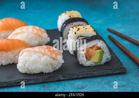 Varietà di nigiri e maki shushi su ardesia e legno bastoncini di pollo su sfondo blu Foto Stock