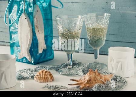 Due bellissimi bicchieri ornamentali di vino bianco con decorazione marina su un tavolo di legno bianco di fronte al blu chiaro sfondo di legno Foto Stock