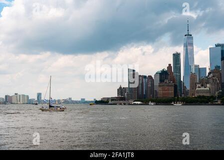 Skyline del centro di Manhattan da Governsnors Island un giorno nuvoloso d'estate. Nave a vela navigazione sul paesaggio urbano di Hudson Reiver agasint. Viaggio a. Foto Stock