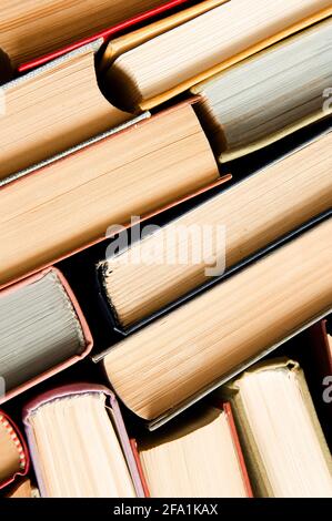 Una pila di libri colorati in una biblioteca o in una stanza. Molti libri spessi multicolore si erigano su uno sfondo scuro. Immagine verticale Foto Stock