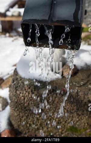 L'acqua gocciola dal tubo discendente dopo che la neve si scioglie in primavera Foto Stock