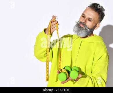 Hipster maturo vecchio brutale uomo bearded in giallo hophodie hold manubri verdi e metro a nastro con elegante barba bianca bianco Foto Stock